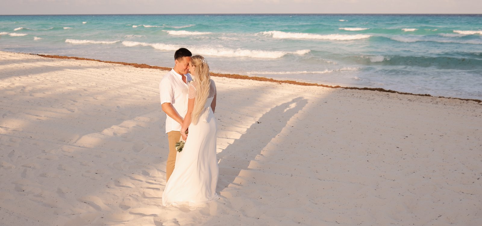 Bajo el resplandor del sol caribeño y el susurro de las olas turquesas, ellos caminan con pasos ligeros sobre la suave arena blanca. Vestidos de blanco, el mar de Cancún es testigo de su amor recién sellado, donde cada ola parece aplaudir su unión. Con cada paso, se adentran en un futuro lleno de promesas brillantes, mientras el cielo despejado y las palmeras les dan la bienvenida a su nueva vida juntos.