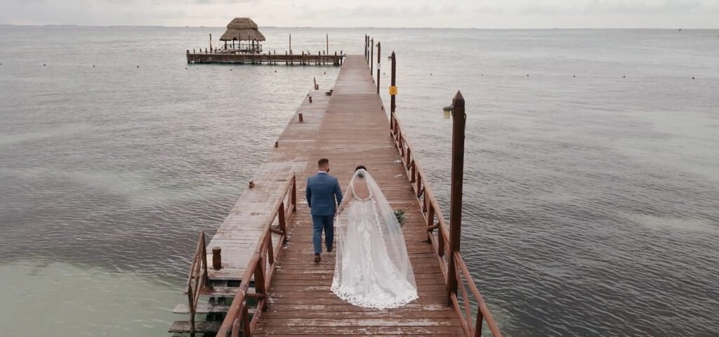 Capturando el momento mágico cuando los recién casados emergen radiantes del muelle, envueltos en la brisa marina y el susurro de las olas. Esta boda en el muelle es el epítome del romance y la elegancia, con el sol poniéndose en el horizonte, pintando el cielo con tonos dorados y rosados. La pareja, deslumbrante en sus atuendos nupciales, refleja la felicidad pura y el amor eterno, mientras sus seres queridos aplauden y celebran este inicio de su nueva vida juntos. Descubre más sobre bodas en muelles y cómo hacer de tu día especial un cuento de hadas inolvidable.